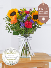 Anniversary Colour Burst - Vase with Free Anniversary Balloon –  Brighten up any room with our "Colour Burst" arrangement, featuring stunning sunflowers, cerise carnations,...