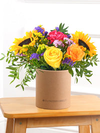 Colour Burst - Hatbox – Brighten up any room with our "Colour Burst" arrangement, featuring stunning sunflowers, cerise carnations,...