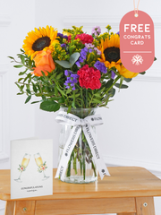 Colour Burst - Vase with Free Congratulations Card – Brighten up any room with our "Colour Burst" arrangement, featuring stunning sunflowers, cerise carnations,...