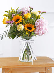 Sweet Meadow Vase – Bursting with the hues of summer, featuring sunflowers, yellow roses, solidago, pink statice, pink...