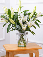 White Lily - Vase – The White Lily in a vase adorned with vibrant eucalyptus and pistach leaves serves...